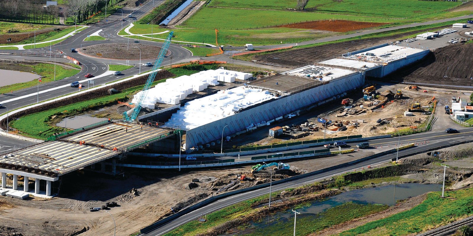 Aerial view of a motorway interchange under construction with white EPS Geofoam blocks stacked inside a bridge approach embankment